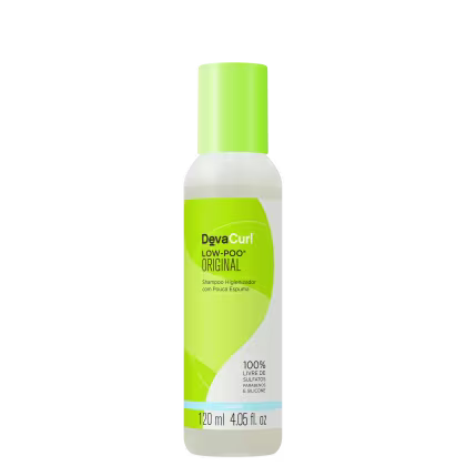 A imagem mostra  o Shampoo Deva Curl Low-Poo Original 120ml.  O frasco é de plástico, com a parte superior verde e a parte inferior branca. As informações no rótulo indicam que o produto é 100% livre de sulfatos, parabenos e silicone.