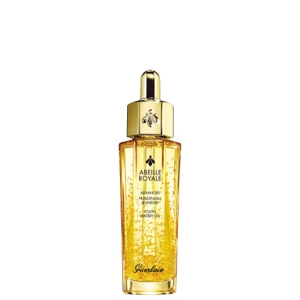 A imagem mostra o frasco do óleo hidratante Abeille Royale da Guerlain. É um frasco de vidro transparente contendo um líquido dourado brilhante, tem um formato cilíndrico alongado com uma tampa dourada na parte superior, com uma abelha estampada.