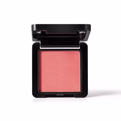 Caixa preta compacta contendo um blush em tom coral vibrante. O produto possui uma tampa preta e uma superfície lisa e uniforme, com uma textura aveludada.