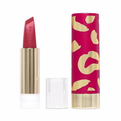 Na imagem há a case de um batom. Ela tem um padrão de manchas abstratas em rosa vibrante e dourado metálico. Esse design moderno e sofisticado com cores vivas é característico de uma linha de cosméticos glam e de luxo.