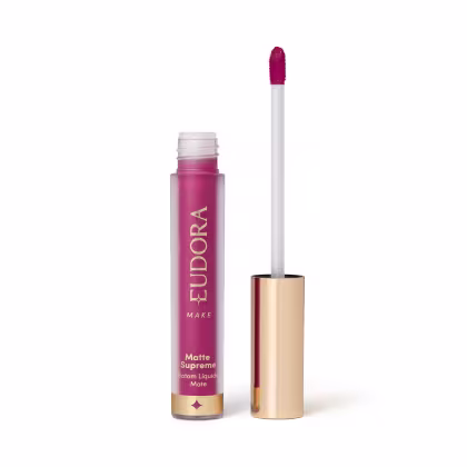 Batom Líquido Matte Supreme em embalagem transparente com tampa dourada e aplicador do tipo bastão. Produto com design minimalista e rótulo dourado no frasco.