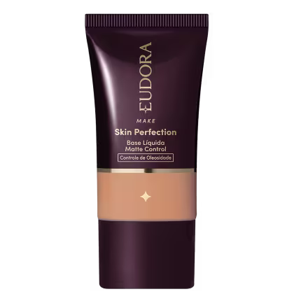 Tubo de base líquida para maquiagem da marca Eudora, com rótulo em tons escuros e dourados, apresentando o nome "Skin Perfection" e informações sobre controle de oleosidade.