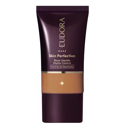 Tubo de base líquida para maquiagem da marca Eudora, com rótulo em tons escuros e dourados, apresentando o nome "Skin Perfection" e informações sobre controle de oleosidade.