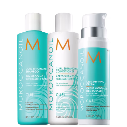 Produtos para cabelos cacheados da linha Moroccanoil Curl. Três embalagens plásticas cilíndricas: um shampoo de 250ml, um condicionadorde 250ml e um creme modelador de cachos de 250ml. As cores predominantes são azul claro, branco e laranja.