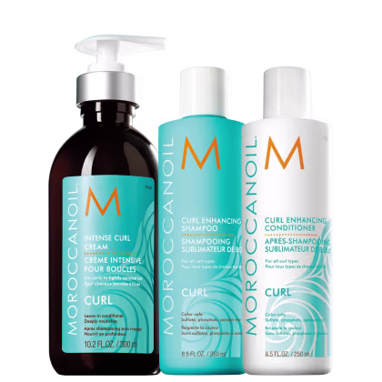 Produtos para cabelos cacheados da linha Moroccanoil Curl. Um creme intensivo de 300ml; um shampoo de 250ml e um um condicionador de 250ml. Todos os frascos exibem o logotipo "M" da marca Moroccanoil. As cores predominantes são turquesa, branco e laranja.