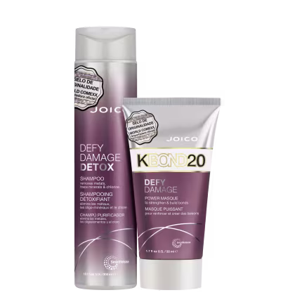 Shampoo e máscara capilar da linha Defy Damage Detox da marca Joico. O shampoo vem em um frasco cilíndrico branco com detalhes em roxo.  A máscara capilar é apresentada em um tubo branco com detalhes roxos.