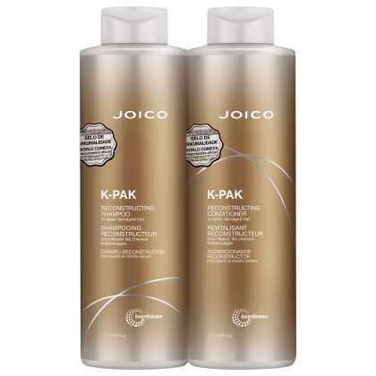 São dois frascos de plástico dourado de 1 litro cada, contendo shampoo e condicionador reconstrutores da linha K-Pak da marca Joico. Os frascos têm formato cilíndrico e tampas brancas.