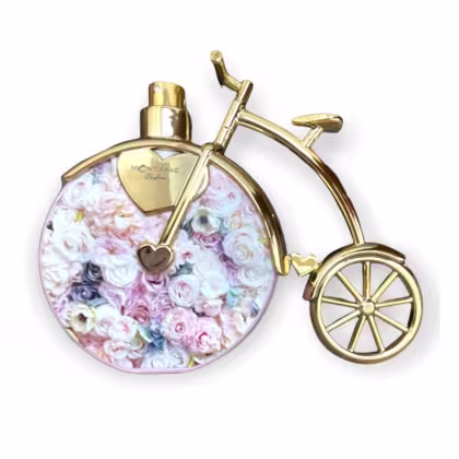 Frasco de perfume Mont'Anne Parfums em formato de bicicleta dourada, com detalhes em coração e roda, sobre fundo floral com rosas em tons pastel.