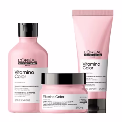 A imagem apresenta a linha Vitamino Color, da L’Oréal Professionnel, para cabelos coloridos: shampoo (frasco), tratamento (pote) e condicionador leave-in (tubo), todos em embalagens rosa claro com tampa preta.