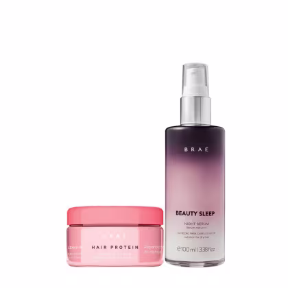O produto é uma linha de cuidados capilares da marca Brae. Há um frasco de vidro transparente roxo escuro a rosa claro, com o rótulo "Beauty Sleep Night Serum". Ao lado, há um pote rosa, com o rótulo "Hair Protein Leave-in".