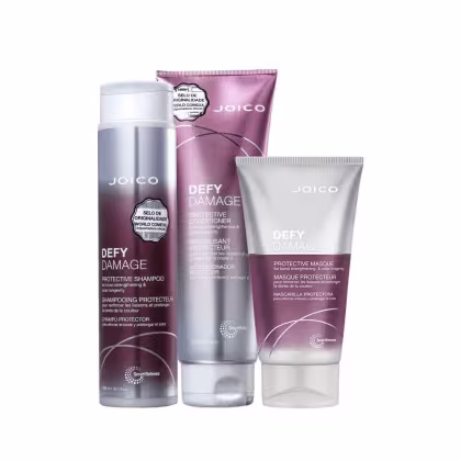 A imagem mostra três produtos da linha "Defy Damage" da marca Joico: shampoo, condicionador e máscara capilar. As embalagens são roxas com tons prateados e letras brancas.