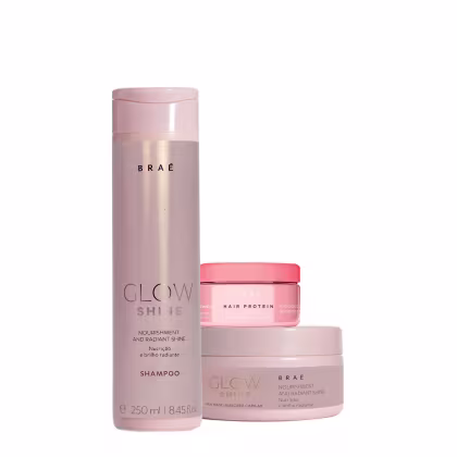Conjunto de produtos da marca Braé, composto por um shampoo, um tratamento capilar e uma máscara capilar. O shampoo vem em uma embalagem cilíndrica rosa claro, O tratamento capilar é um pote rosa e a máscara capilar é um pote rosa claro com a inscrição.