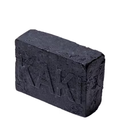 Barra de sabonete vegetal artesanal de cor preta. A barra tem formato retangular com cantos arredondados. A superfície apresenta textura áspera e irregular, com sulcos e relevos que parecem ser inscrições ou símbolos esculpidos.
