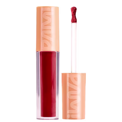 A imagem mostra o batom líquido matte de Pam by Pamella. Seu tubinho é transparente e mostra a cor vermelha do batom. Ao lado tem a tampa laranja com a logo PAM! escrita e o bastão com uma ponta de aplicador em formato de ampulheta.