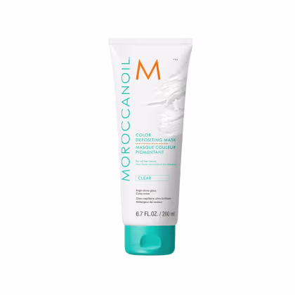 A imagem mostra a embalagem do produto Moroccanoil Color Depositing Clear Mask 200ml, um tubo plástico branco com detalhes em verde e laranja. O produto é descrito como uma máscara pigmentada que proporciona brilho intenso aos cabelos e revive a cor.