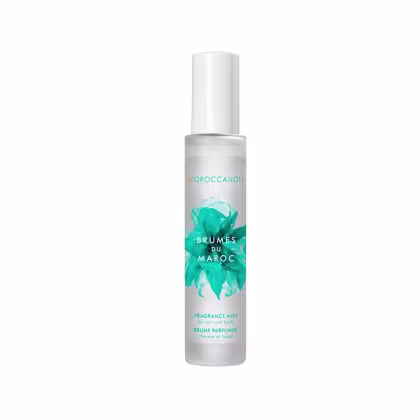 A imagem mostra o produto Moroccanoil Brumes du Maroc 100ml.  O rótulo indica que é um "Fragrance Mist" (Bruma Perfumada). O design do rótulo apresenta folhas estilizadas de tom turquesa sobre um fundo branco, dando uma aparência inspirada na natureza.