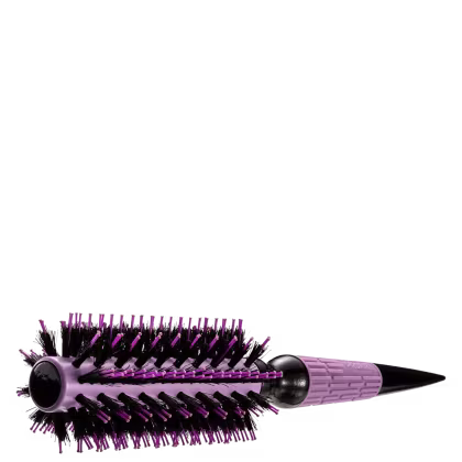 A imagem mostra uma escova de cabelo. O produto tem um cabo longo e cilíndrico na cor roxa. A escova possui cerdas de nylon rígidas e densas, também na cor roxa. A base da escova é preta e pontiaguda com detalhe em lavanda.