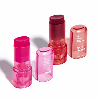 Produtos de maquiagem da marca Quem Disse, Berenice? em embalagens plásticas translúcidas nas cores rosa e vermelho, incluindo um batom, um blush em bastão e um produto de acabamento.