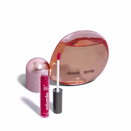 Frasco de perfume Desobediente da marca Quem Disse, Berenice? com tampa rosada e líquido vermelho, acompanhado de um batom líquido da mesma marca na cor rosa.