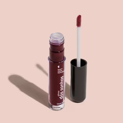 Frasco cilíndrico transparente contendo um gloss labial roxo. Rótulo na embalagem com o nome do produto "Gloss dos Sonhos" e a descrição "Quem disse, berence?". Ao lado, a tampa preta do produto, que acompanha um aplicador de espuma.