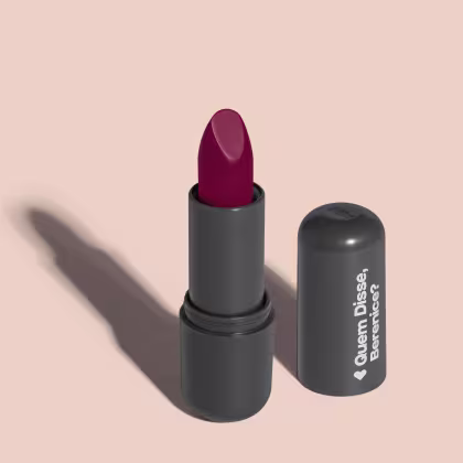 O produto apresentado na imagem é um batom da marca Quem Disse, Berenice?. O batom possui uma embalagem preta fosca e o produto em si é de uma cor rosa. O rótulo na embalagem exibe o nome da marca em branco.