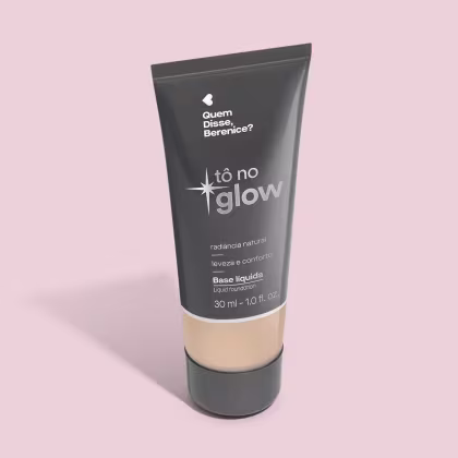 O produto apresentado é uma base líquida da marca Tô no Glow, com embalagem em tubo plástico preto e branco. O rótulo exibe o nome da marca e a descrição "Radiância natural, leveza e conforto". O produto é classificado como "Base líquida".