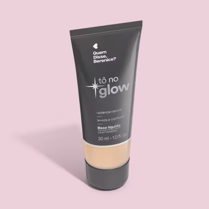 O produto apresentado é uma base líquida da marca Tô no Glow, com embalagem em tubo plástico preto e branco. O rótulo exibe o nome da marca e a descrição "Radiância natural, leveza e conforto". O produto é classificado como "Base líquida".