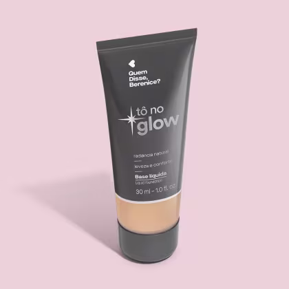 O produto apresentado é uma base líquida da marca Tô no Glow, com embalagem em tubo plástico preto e branco. O rótulo exibe o nome da marca e a descrição "Radiância natural, leveza e conforto". O produto é classificado como "Base líquida".