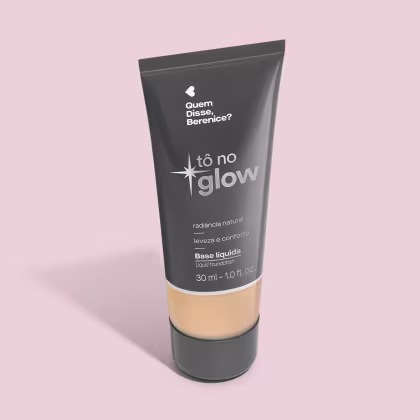 O produto apresentado é uma base líquida da marca Tô no Glow, com embalagem em tubo plástico preto e branco. O rótulo exibe o nome da marca e a descrição "Radiância natural, leveza e conforto". O produto é classificado como "Base líquida".