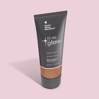 O produto apresentado é uma base líquida da marca Tô no Glow, com embalagem em tubo plástico preto e branco. O rótulo exibe o nome da marca e a descrição "Radiância natural, leveza e conforto". O produto é classificado como "Base líquida".