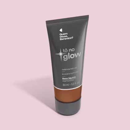 O produto apresentado é uma base líquida da marca Tô no Glow, com embalagem em tubo plástico preto e branco. O rótulo exibe o nome da marca e a descrição "Radiância natural, leveza e conforto". O produto é classificado como "Base líquida".