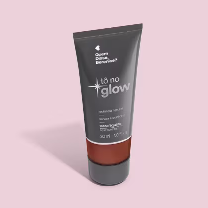 O produto apresentado é uma base líquida da marca Tô no Glow, com embalagem em tubo plástico preto e branco. O rótulo exibe o nome da marca e a descrição "Radiância natural, leveza e conforto". O produto é classificado como "Base líquida".