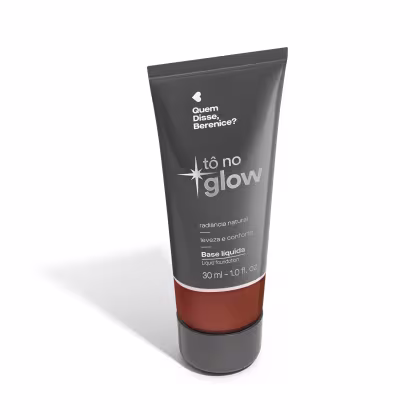 O produto apresentado é uma base líquida da marca Tô no Glow, com embalagem em tubo plástico de cor cinza escura. O rótulo exibe o nome da marca e o texto "Radiância natural, leveza e conforto" em letras brancas.