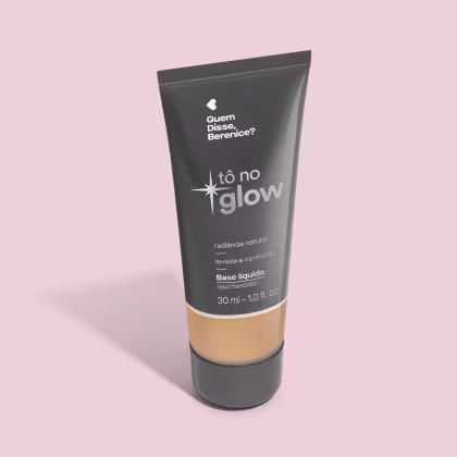O produto apresentado é uma base líquida da marca Tô no Glow, com embalagem em tubo plástico preto e branco. O rótulo exibe o nome da marca e a descrição "Radiância natural, leveza e conforto". O produto é classificado como "Base líquida".