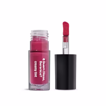 Frasco de gloss labial da marca Quem Disse, Berenice? em tom de rosa vibrante, com aplicador em formato de pincel vermelho. Embalagem preta e branca com texto destacado.