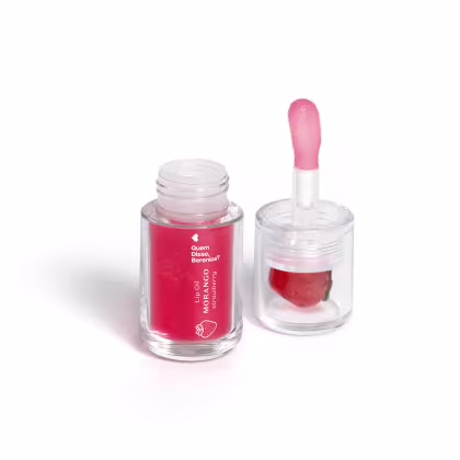 Frasco de lip oil com rótulo em vermelho e rosa, contendo um aplicador em formato de coração. Produto da marca Guem disse, Berenice, com a descrição "Lip Oil Morango" na embalagem.