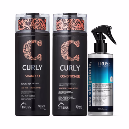 A imagem mostra três produtos. São um shampoo e um condicionador da linha Curly, ambos em embalagens pretas de 300ml, com detalhes em rosa. E um tratamento spray Uso Obrigatório em uma embalagem de 260ml, nas cores preta e azul.
