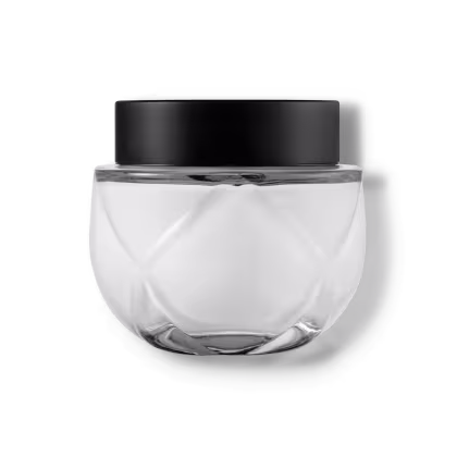 Frasco de vidro transparente arredondado com tampa preta. O recipiente tem uma forma esférica achatada. A tampa preta opaca contrasta com o vidro transparente do frasco que contém o creme na cor branca.