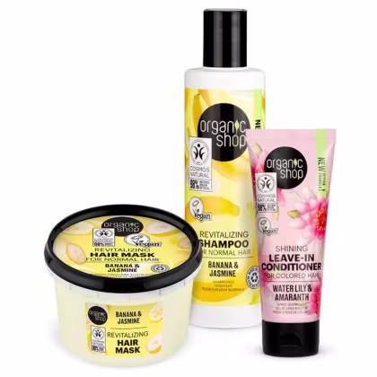 A imagem mostra shampoo em frasco plástico branco com rótulo amarelo e preto, contendo imagens de banana. Máscara capilar revitalizante redonda amarela com rótulo preto. Leave-in em frasco plástico rosa com rótulo preto.