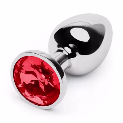 O produto apresentado é um plug anal de metal com uma gema vermelha incrustada na extremidade. O corpo do plug é prateado e liso, com uma base alargada para maior segurança e conforto durante o uso.