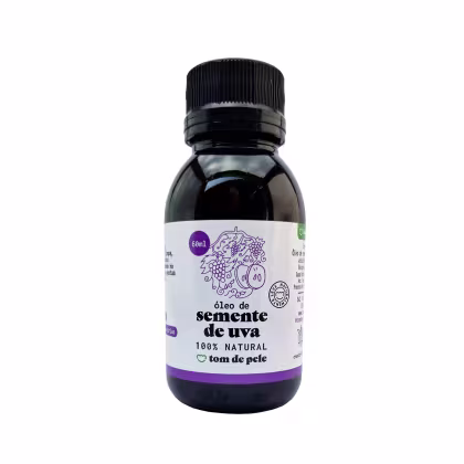 Óleo de semente de uva da marca Tom de Pele. O frasco é de vidro escuro com um rótulo branco e roxo, contendo informações sobre o produto, como o nome "óleo de semente de uva" e a indicação de ser 100% natural.