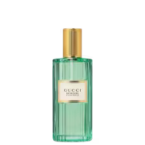 A imagem mostra um frasco de perfume retangular e feito de vidro transparente na cor verde esmeralda. Possui tampa cilíndrica dourada e na frente do frasco, uma etiqueta retangular bege com o nome da marca em destaque e, abaixo, o nome do perfume.