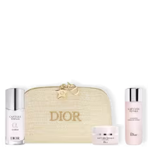 Nécessaire dourada com a palavra "Dior" na frente. Uma loção facial em formato cilíndrico na cor rosa claro e tampa dourada.  m sérum redutor de linhas em embalagem cilíndrica prateada. Pote de creme redutor de linhas redondo nas cores prateada e branco.