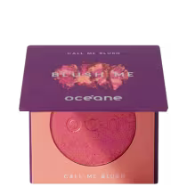 A imagem mostra o produto Blush Me da marca Océane. É uma embalagem quadrada de cor roxa que está semiaberta mostrando a cor do blush em um tom laranja com leve brilho perolado. A parte interna da embalagem é de cor pêssego claro,