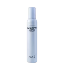 A imagem mostra a Mousse Keune Cashmere Cloud em frasco branco fosco. Embalagem cilíndrica com tampa protetora na cor azul claro. Nome do produto "Cashmere Cloud" e a marca "Keune" em letras pretas. Descrição adicional "Dry volumizing mousse"