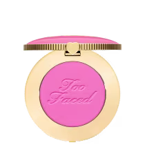 Blush compacto de maquiagem com embalagem redonda dourada. A tampa superior é rosa com a inscrição "Too Faced" em letras cursivas. Um pequeno coração dourado adorna o centro da tampa.