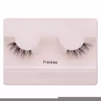 A imagem mostra os cílios postiços em um estojo plástico claro. O estojo tem uma cor nude claro e exibe um par de cílios postiços pretos.