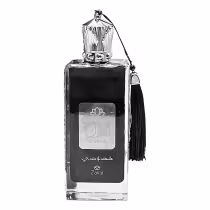 Frasco de perfume de vidro transparente com tampa decorativa e borla preta. Rótulo preto com logotipo da marca Zakat e texto em árabe. Produto de beleza com design elegante e sofisticado.