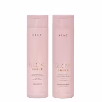 Dois frascos de produtos Braé da linha Glow Shine, um de shampoo e outro de condicionador, com embalagens rosadas e textos em dourado indicando os nomes dos produtos.