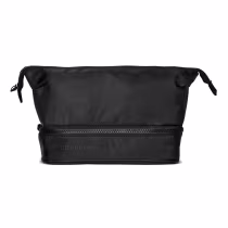 Possui um design simples e minimalista, com um zíper principal e um bolso frontal. A bolsa é feita de material resistente e tem um acabamento liso. O logotipo da marca O Boticário está impresso na parte frontal da bolsa, em uma cor preta discreta.
